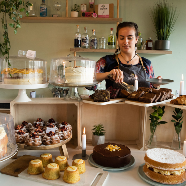 A woman works behind a counter cover in cakes of all different shapes and sizes.