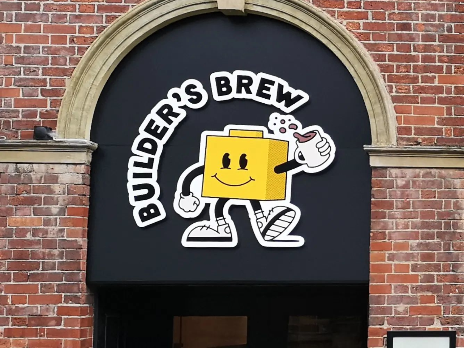 Builder's Brew Café logo on the outside of a building. The logo has the words 'Builder's Brew' round a cartoon character, who is shaped like a toy building brick, holding a mug of tea.