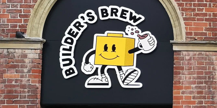 Builder's Brew Café logo on the outside of a building. The logo has the words 'Builder's Brew' round a cartoon character, who is shaped like a toy building brick, holding a mug of tea.