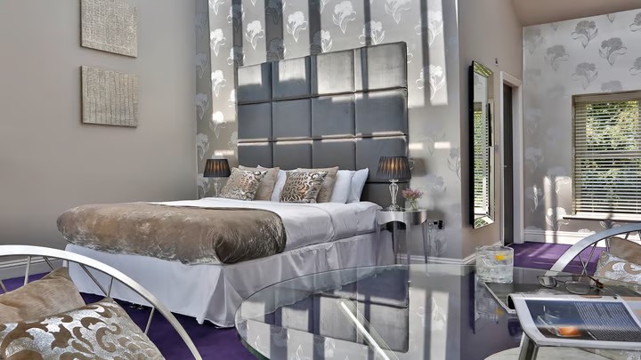 Opulent hotel bedroom at Aston Hall Hotel with king-size bed, cushions, and warm lighting creating a relaxing ambiance.