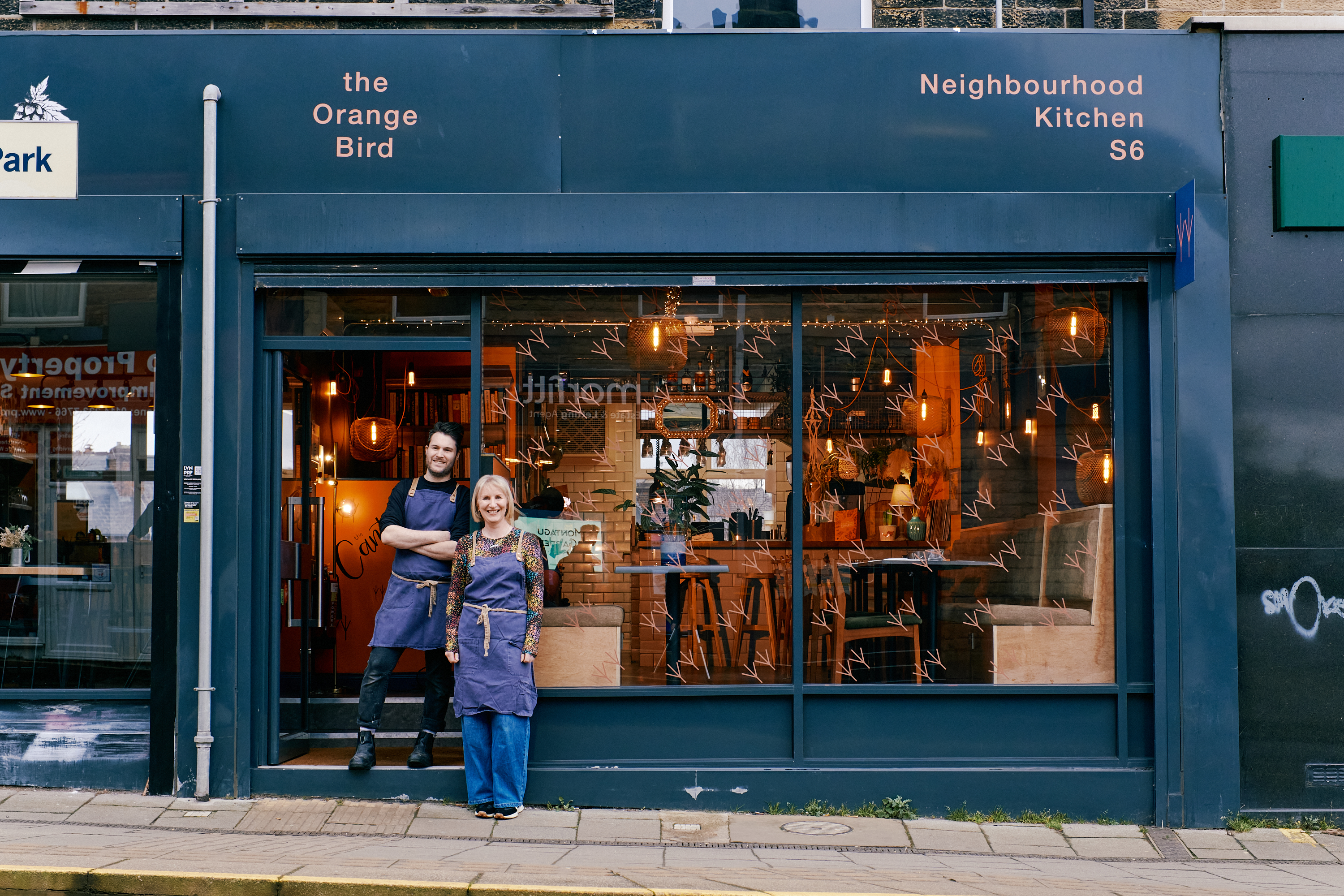 Front view of The Orange Bird restaurant at during the day with two friendly owners standing out front ready to welcome you 