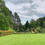 A view across a grassy area in Whirlow Brook Park, that is banked by well-tended boarders, hedges and trees.
