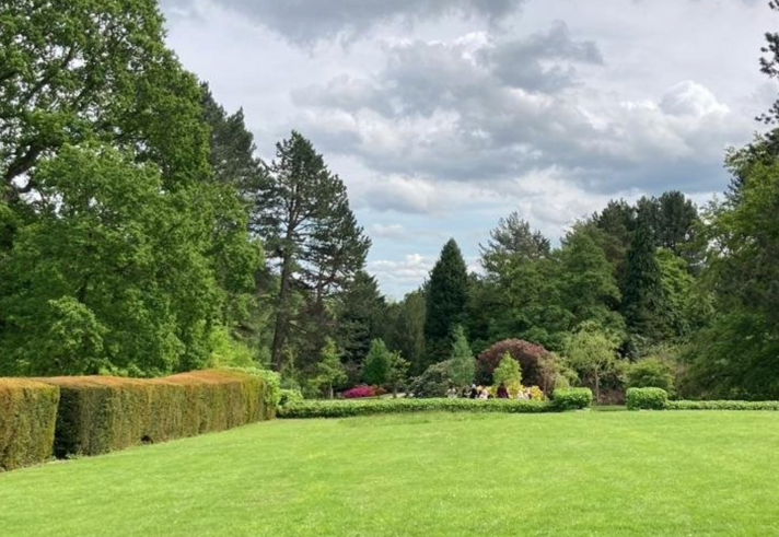 A view across a grassy area in Whirlow Brook Park, that is banked by well-tended boarders, hedges and trees.