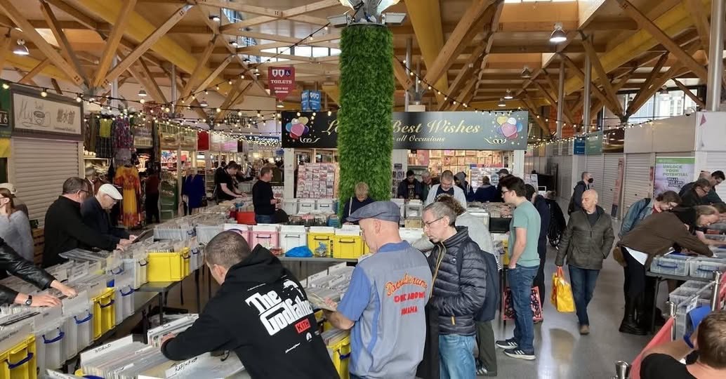 A record fair in full swing with people looking through boxes of records.