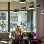 Female working in bar area with tables and chairs and overhead pendant lights.