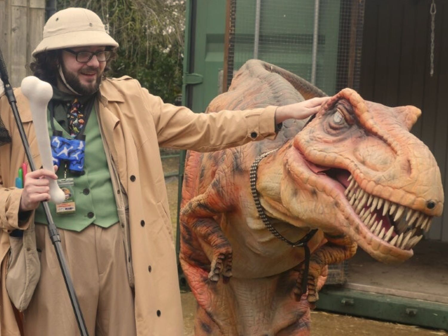 A man in a pith helmet stands next to a model dinosaur.