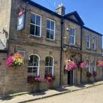 The Old Horns Inn photographed on a sunny day, showcasing its traditional stone façade, arched windows, colourful hanging baskets and cobbled street setting.