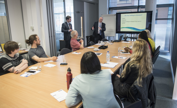 Workshop attendees sit round a large table in a modern office watching a presentation. 