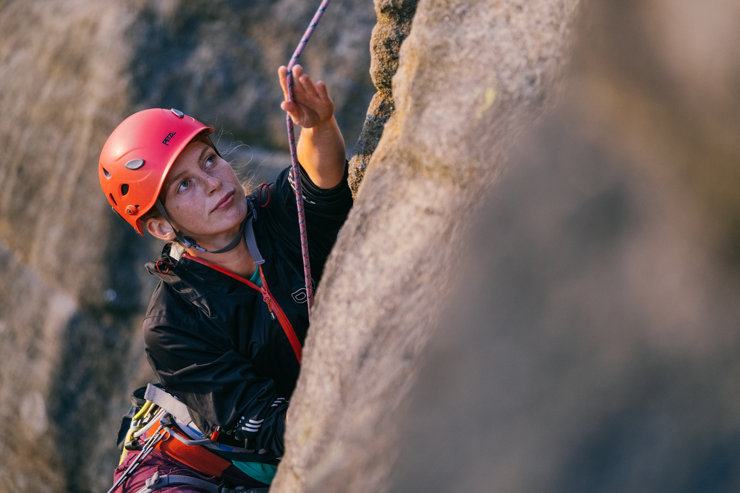 A woman climbing a gritstone rock face.