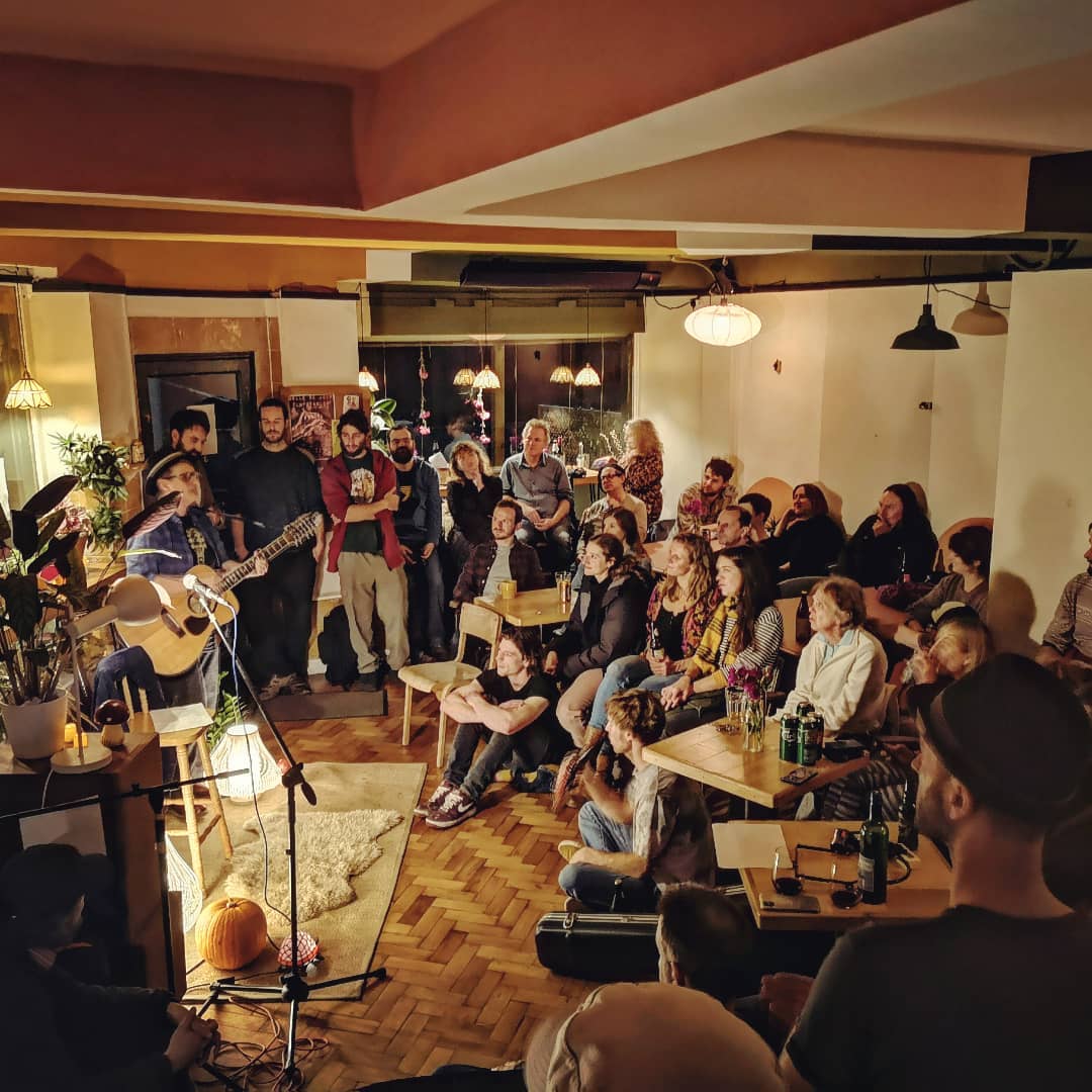A man plays an acoustic guitar and sings in front of a small crowd at Kopi & Chai.