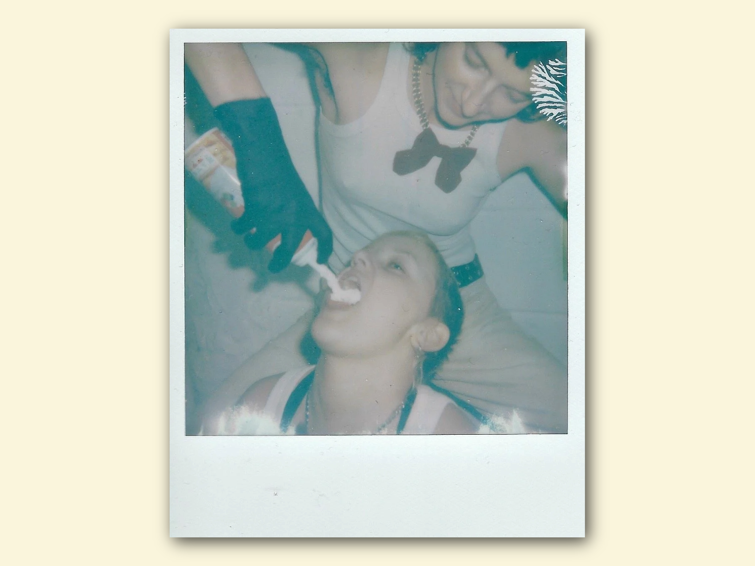 A Polaroid style picture of a person squirting canned cream into another persons mouth. 