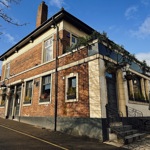 The exterior of The Lescar pub, a traditional brick building with cream detailing, large windows and hanging plants, photographed on a bright day.