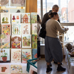 Two people looking at a craft stall at an indoor market.