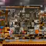 The bar at Guzzle with several beer pumps, a large blackboard with drinks and prices and shelves filled with bottles.