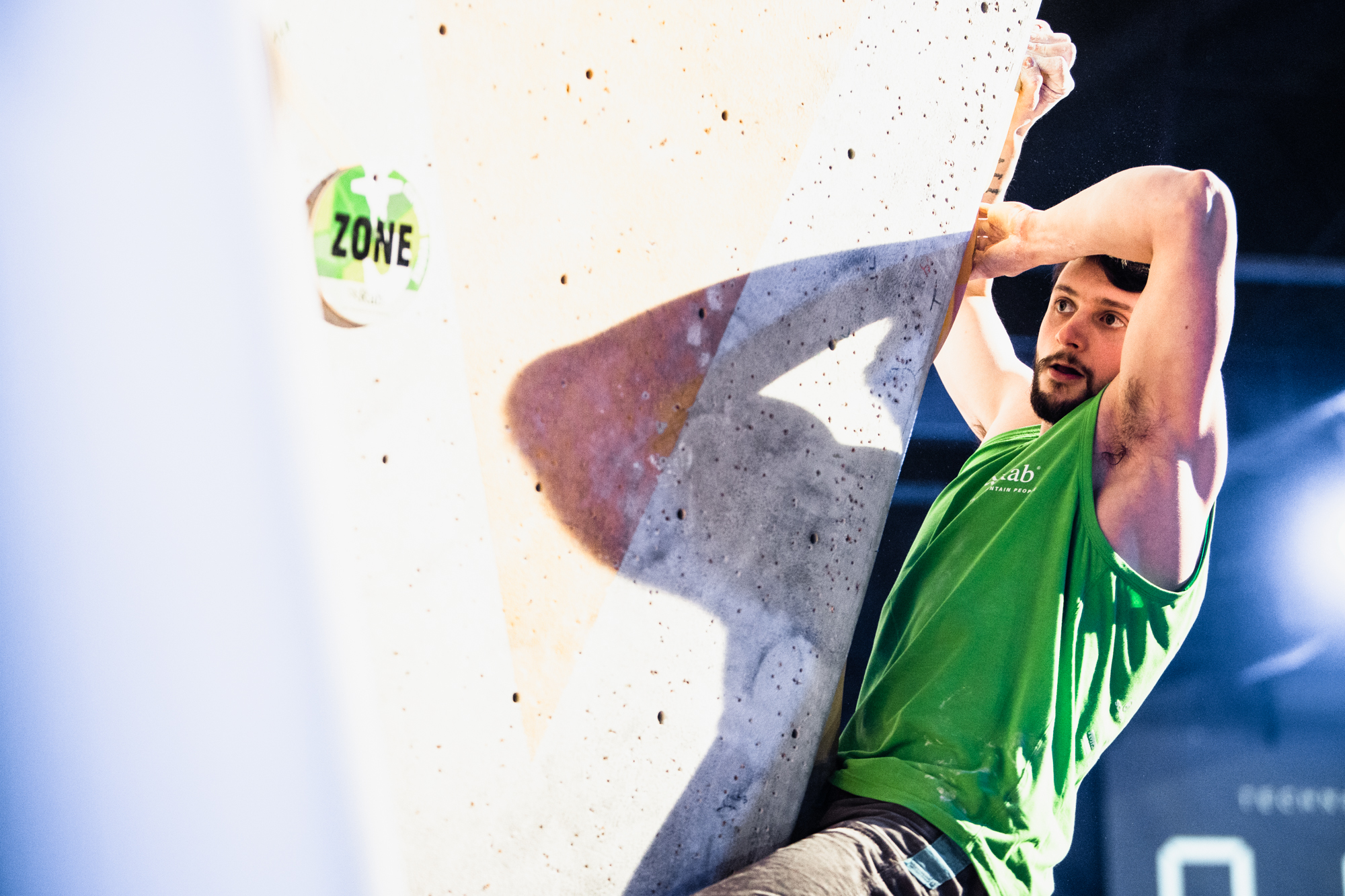 A man is climbing on the corner of a wall. He has one hand holding onto the wall vertically and another held onto the wall horizontally.
