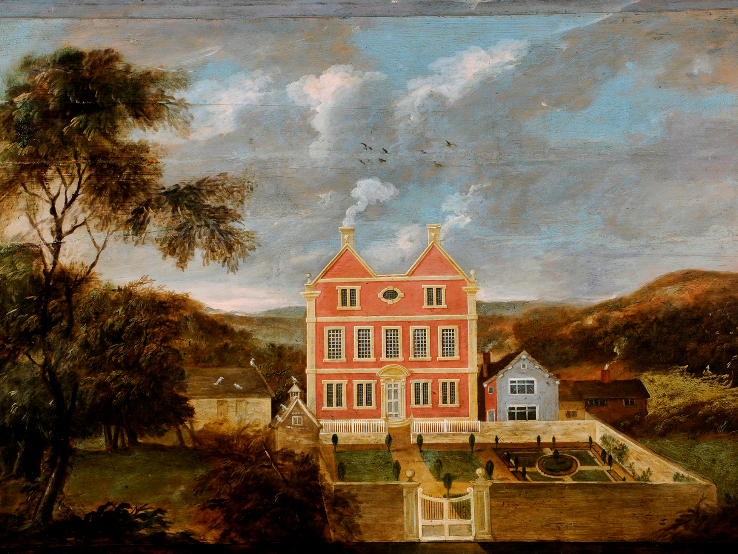 An 18th-century painting of a large red-brick Georgian house with white trim and two chimneys, set in a formal walled garden with symmetrical paths and topiary. Smaller buildings stand nearby, surrounded by trees and rolling hills under a partly cloudy blue sky. A white gate leads into the garden, and birds are visible flying in the distance.