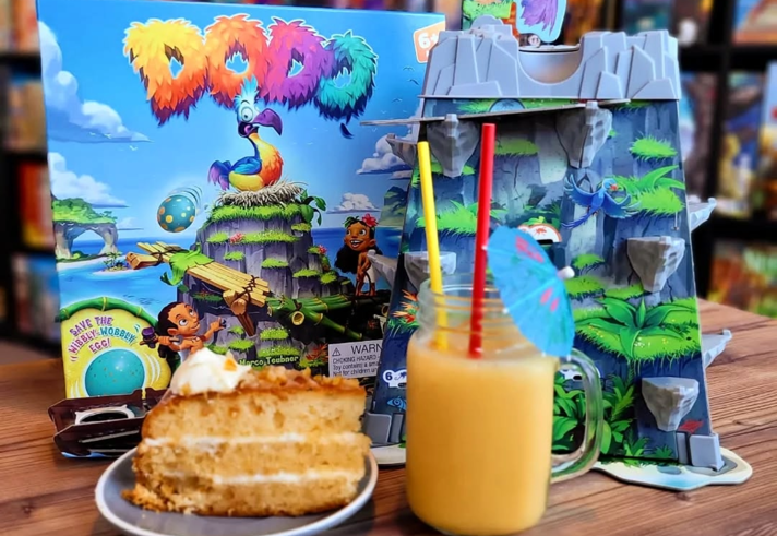 A table at The Dice Box Sheffield with a cocktail, a slice of cake and a game called Dodo.
