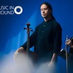 Two musicians stand in front of a rippling blue background holding their instruments.