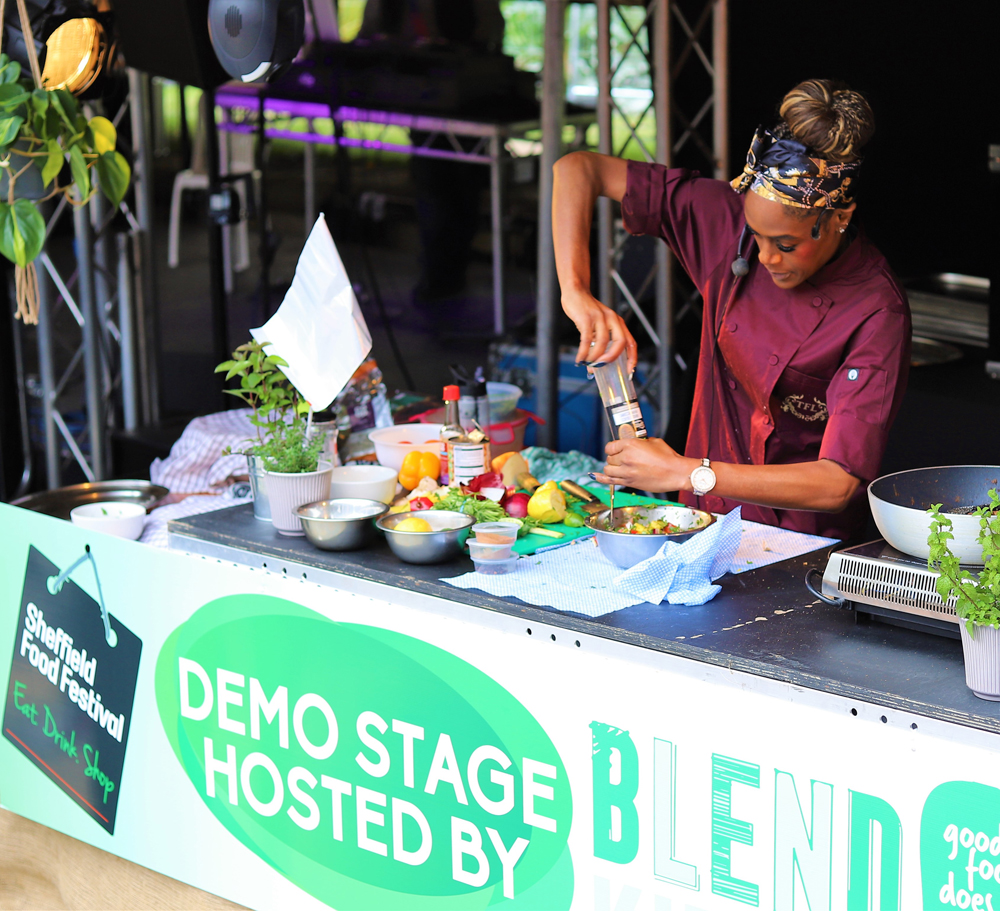 A chef leads a cooking demonstration from a stall as she's seasons a dish 