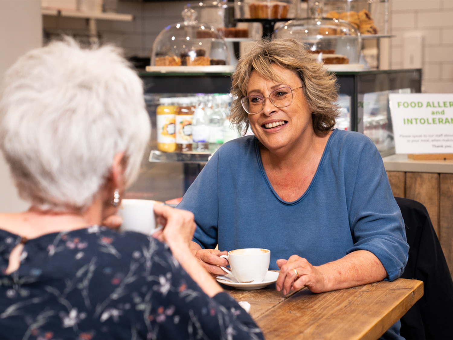 Two women sit at a table, drinking coffee and chatting.