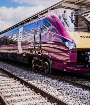 EMR Gold Award 222 - Modern maroon and cream-colored passenger train with the number 222104 parked at a station platform. The train has a sleek aerodynamic design with reflective windows, and the station features a covered roof structure with metal beams. Bright daylight and partly cloudy skies are visible in the background.