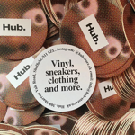 A close-up of a pile of Hub. merchandise stickers. In the middle is a white circle with the words 'VINYL, SNEAKERS, CLOTHING AND MORE'.