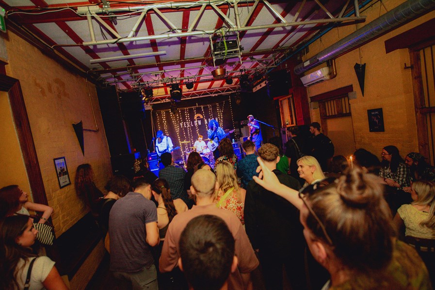 A view from the back of a crowd as they watch a lively band perform on the Yellow Arch stage