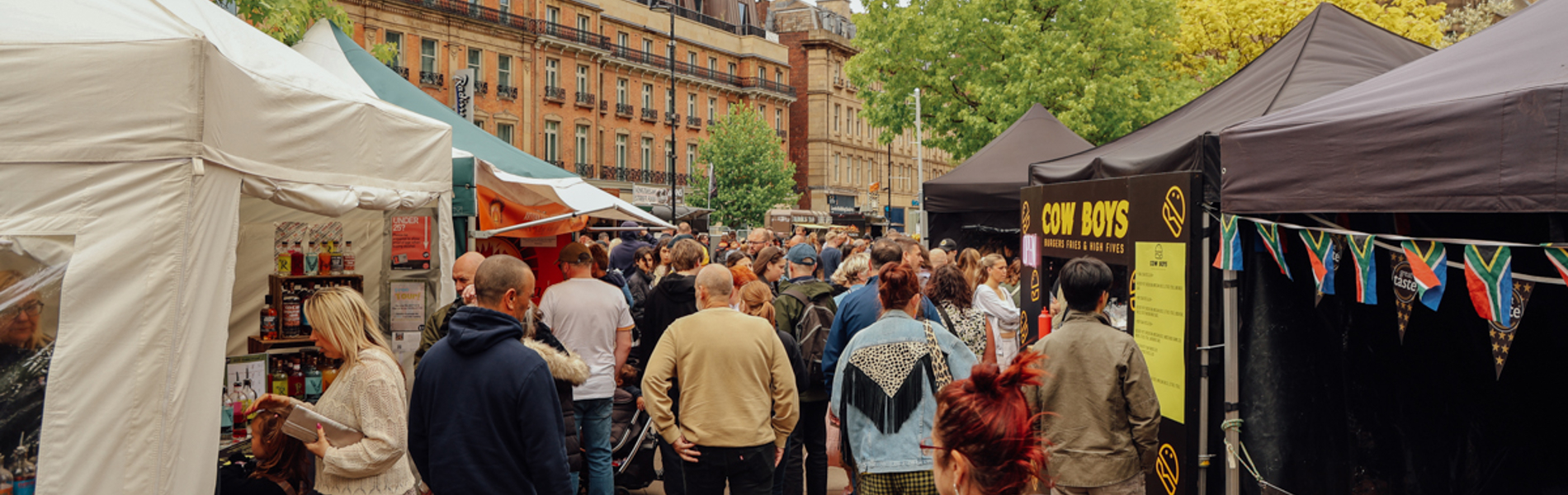 Crowds walking through an outdoor market lined with food stalls and tents in a city square