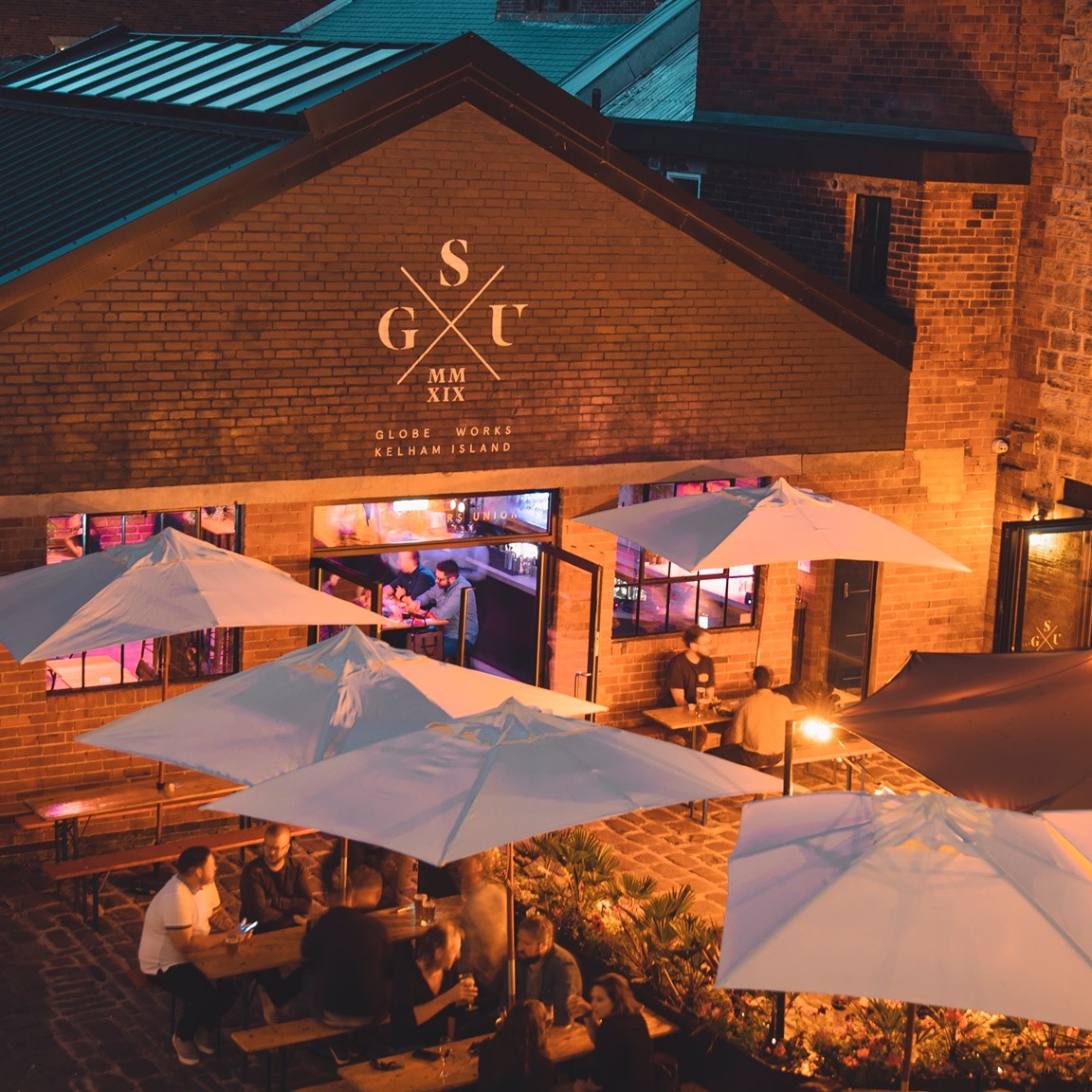People eating at tables outside Saw Grinders Union at night.