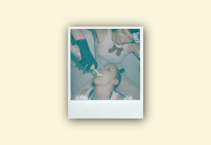 A Polaroid style picture of a person squirting canned cream into another persons mouth. 