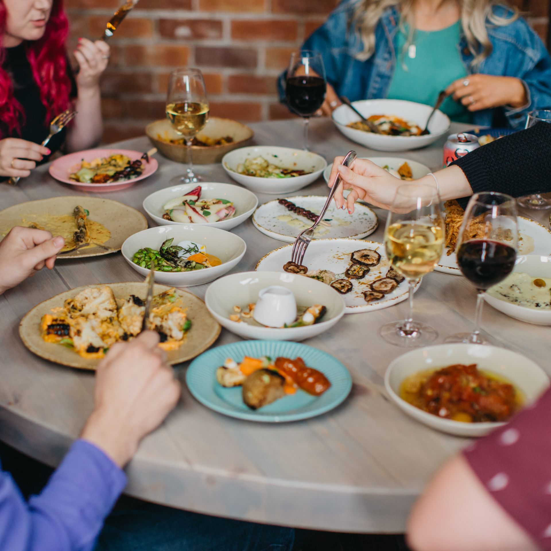 A table at a restaurant covers in lots of small plates of food. Five people are sat round enjoying the meal.