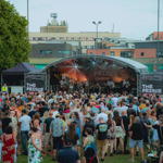 Shot from the back of a large crowd of people as they stand in front of the Devonshire Green Stage watching a band perform