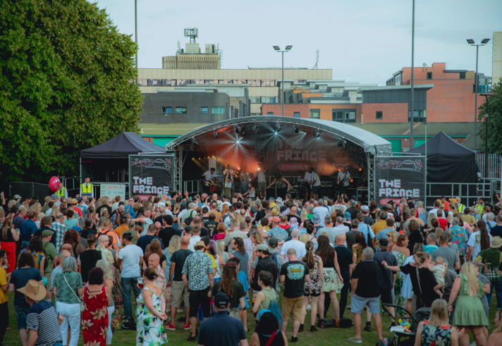 Shot from the back of a large crowd of people as they stand in front of the Devonshire Green Stage watching a band perform