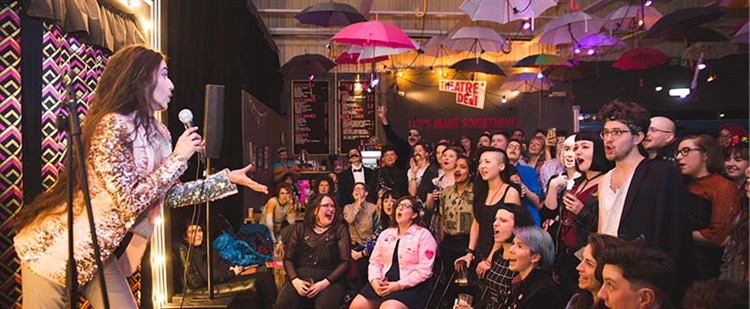 An entertainer on stage performing in front of a crowded room at Theatre Deli.