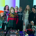A group of people standing behind DJ decks.