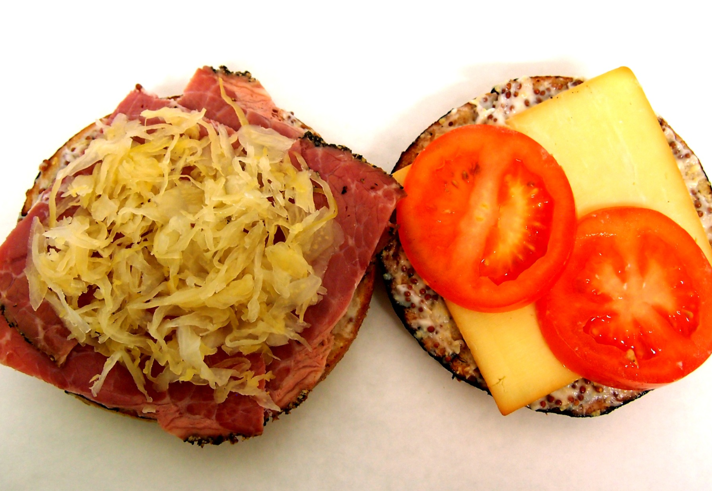 A bagel filled with pastrami, sauerkraut, cheese and tomato.
