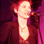 Emily Maguire singing on stage with an acoustic guitar. 