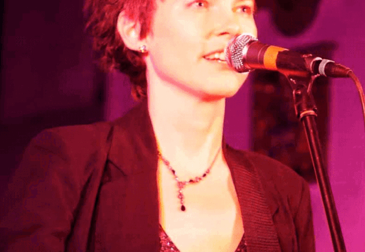 Emily Maguire singing on stage with an acoustic guitar. 