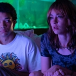 A still from the film "I Saw The TV Glow": two young people are sat on a sofa in a dimly lit room.