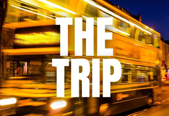 A motion blurred image of a double decker bus at might, with the words 'THE TRIP' overlaid on the centre of the image in bold white text.