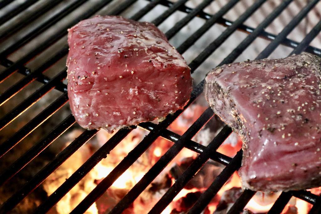 Two steaks on a charcoal grill.