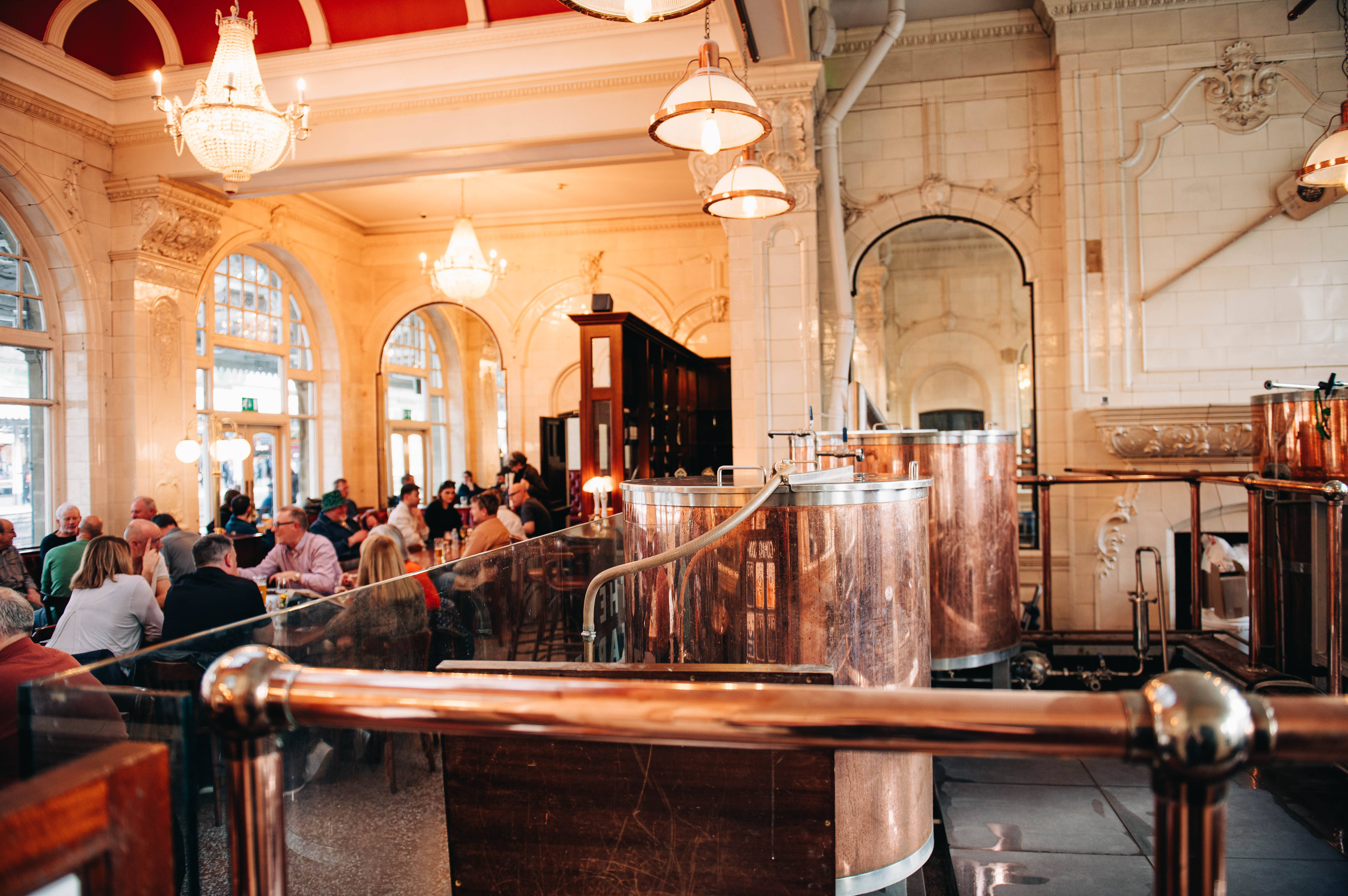 Sheffield Tap copper beer tanks to the right, with groups of people sat down talking and drinking to the left.