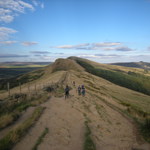 A rough track winding through hills in the countryside. In the distance you can see various groups of people out walking.