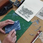 A close up of someone carving lino to make a print of a flower.