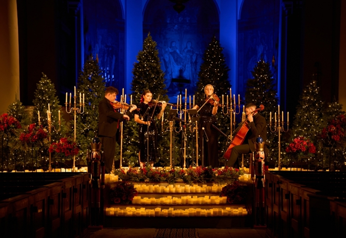 A string quartet performs on a stage, surrounded by many candles.