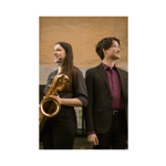 Two young musicians stand back-to-back outdoors in front of a brick building, smiling and looking in opposite directions. One holds a large saxophone and wears a dark outfit, while the other wears glasses and a dark suit with a burgundy shirt. The warm-toned portrait highlights the performers and their instruments in a relaxed, professional setting.