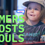 Promotional graphic for “Gamers, Ghosts + Ghouls” featuring a child wearing a cap and sitting at a gaming station. Large bright green text fills the left side of the image, while a pixel-style speech bubble saying “Boo!” appears above. A game controller is visible in the foreground, with another person holding a controller at the right edge. The softly blurred background shows screens and arcade-style equipment, combining gaming and Halloween themes.