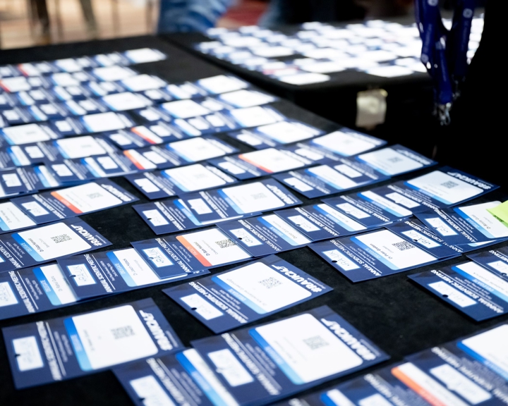 Table covered with numerous blue and white delegate badges arranged in rows, each featuring a name, QR code, and event branding.