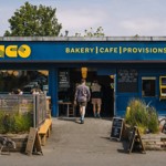 The exterior of a building painted blue. There is yellow lettering above the window and door that reads ' Tonco' and 'Bakery, Cafe, Provisions'.
