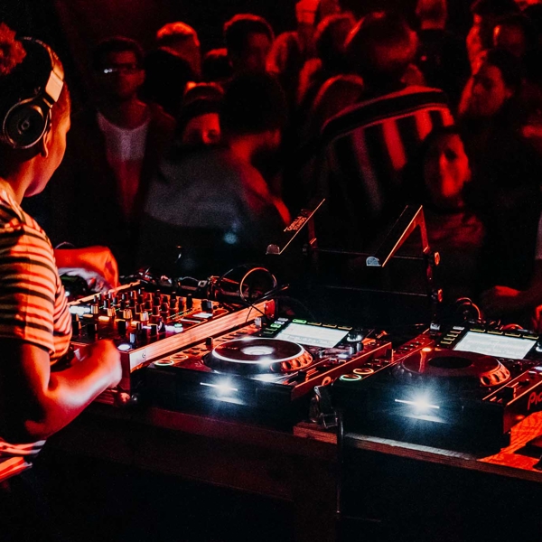 A female DJ of African heritage is mixing at the decks, for a nightclub crowd.